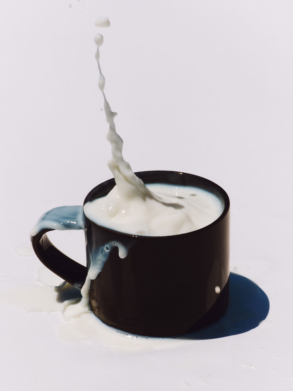 Milk splashing out of a black mug on a white surface.